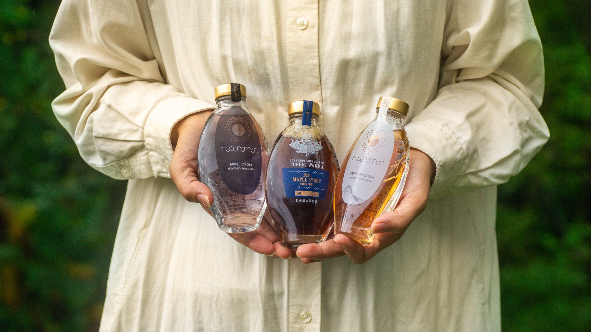 北海道メープルシロップ「トペニワッカ」とルプノモリシリーズのクラフトジン「TSUKI」とクラフトリキュール「HI」を手に持つ女性